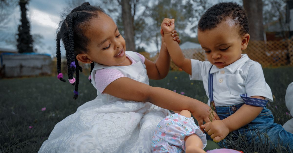 Two young children playing happily with toys outdoors in a sunlit garden.